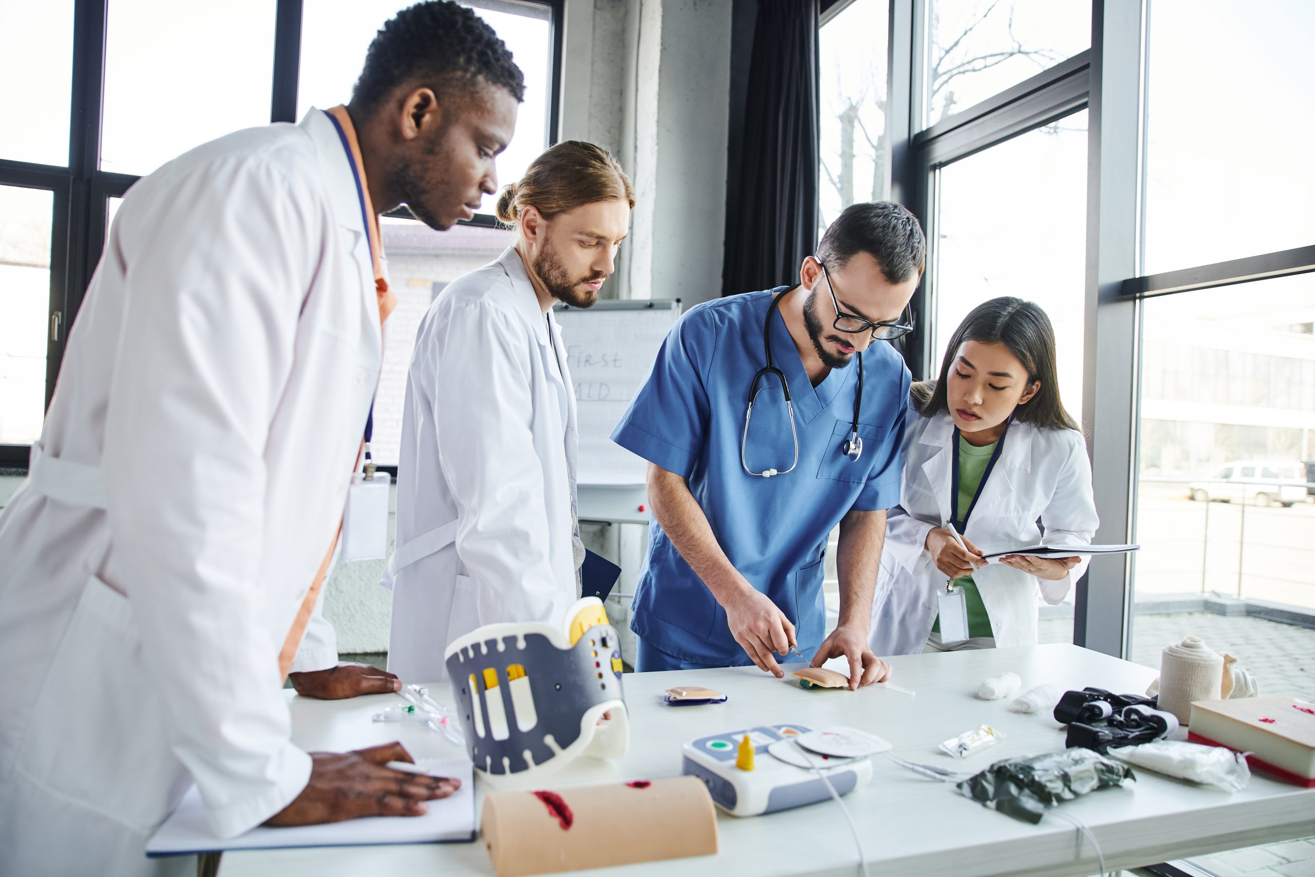 doctor in uniform and eyeglasses making injection in training pad near medical equipment and students in white coats