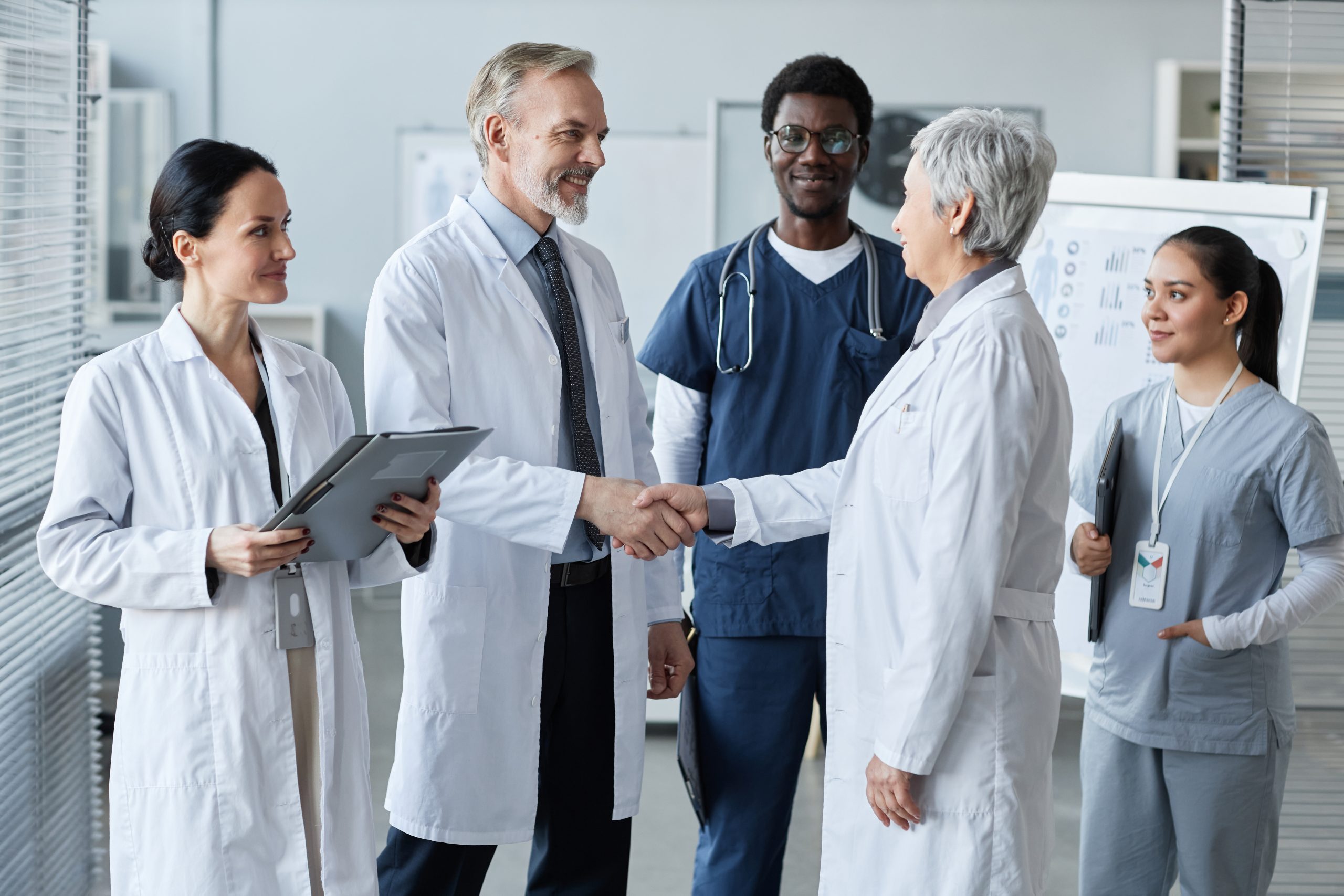 male general practitioner shaking hand of female colleague amongst other medical staff